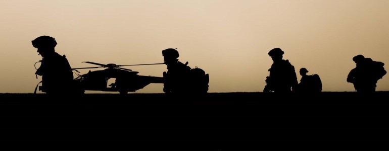 Silhouettes of soldiers patrolling with helicopter in background