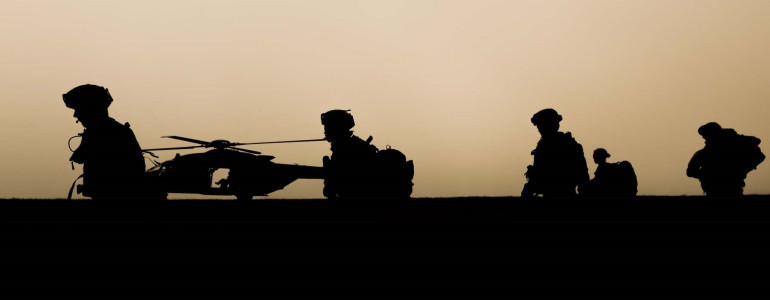 Silhouettes of soldiers patrolling with helicopter in background