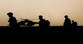 Silhouettes of soldiers patrolling with helicopter in background