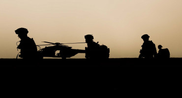 Silhouettes of soldiers patrolling with helicopter in background