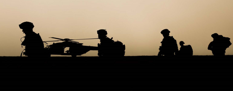 Silhouettes of soldiers patrolling with helicopter in background