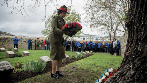 A woman in army uniform laying a wreath at the base of a tree in a cemetery 