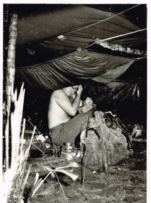 Bill in the jungle sending a message by morse code. On his knee is a radio battery and he’s holding a morse code sending key.