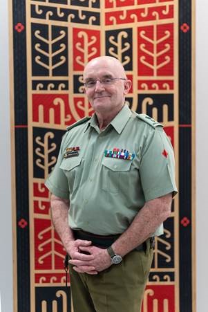 Derrick in a decorated Army uniform in front of a Māori kōwhaiwhai pattern