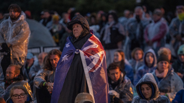 A woman standing amongst a crowd, draped in a New Zealand flag