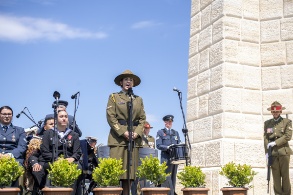 A woman in army uniform singing in front of a memorial