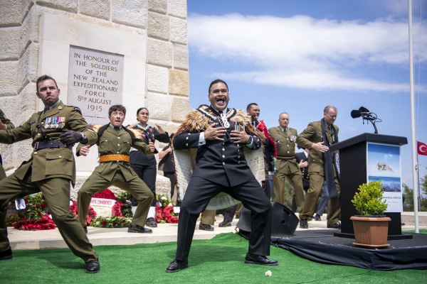 Uniformed personnel performing a haka in front of a memorial statue
