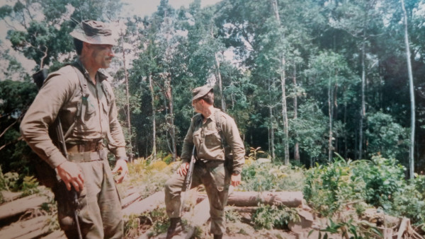 Two men standing in army uniforms standing in the clearing of a jungle