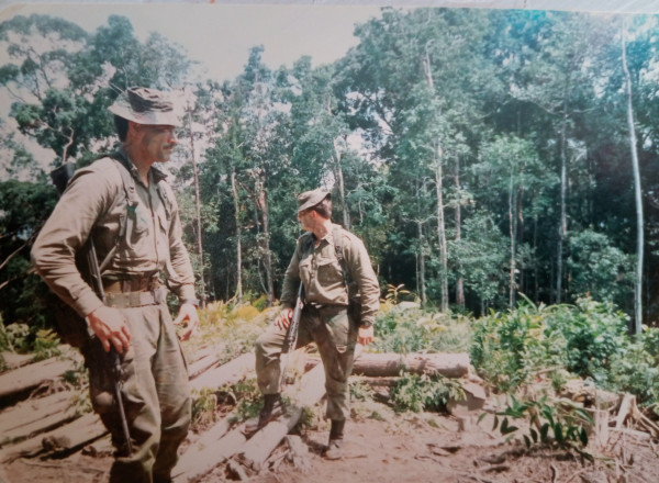 Two men in army combat uniforms stand in a jungle clearing