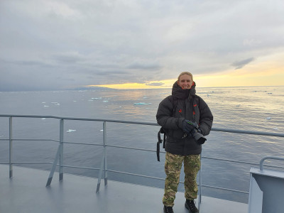 Maria in army uniform holding her camera on the deck of a ship in the Antarctic Ocean