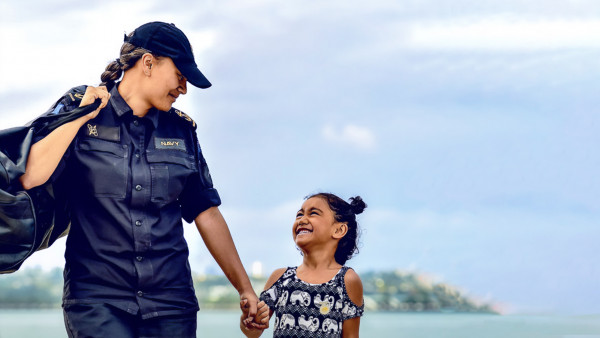 A woman in Navy uniform holding the hand of a smiling young girl