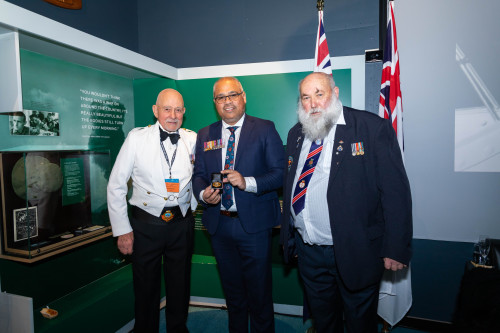 Three men in suits with medal racks in a museum 