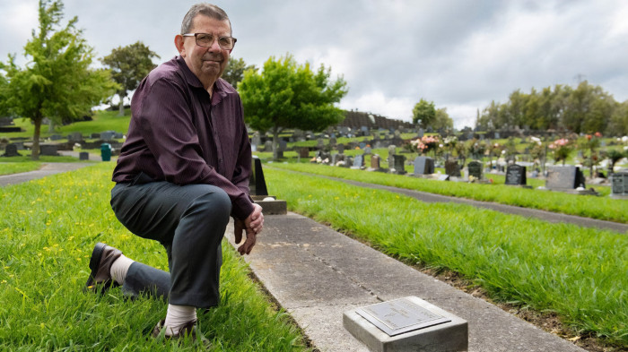 Barry Rankin kneeling at a memorial plaque in a cemetery