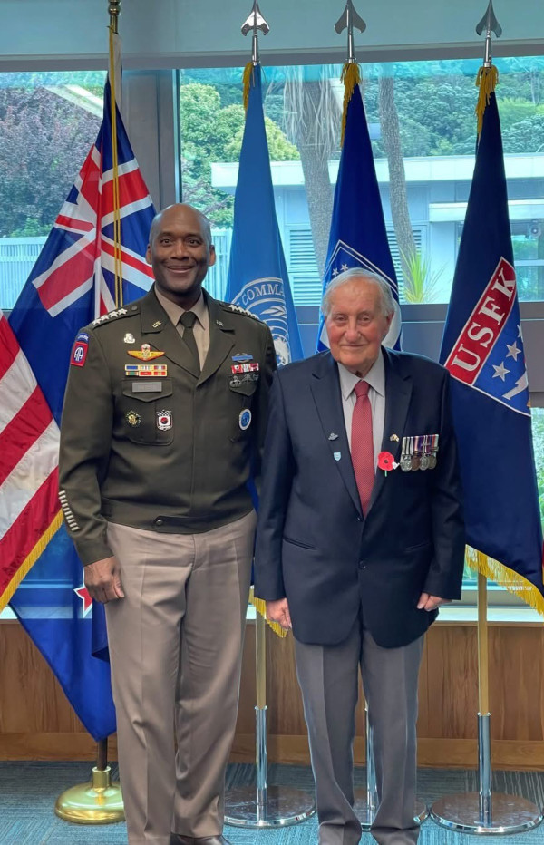 A middle aged US Army General in uniform stands next to 90-year-old Phil Wallace wearing a suit with a medal rack. 