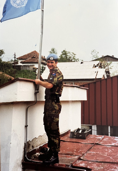 A woman in Army uniform raising a flag at a flagpole on top of a roof