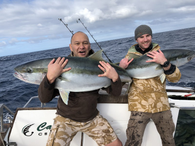 Two men holding large fish caught on a boat