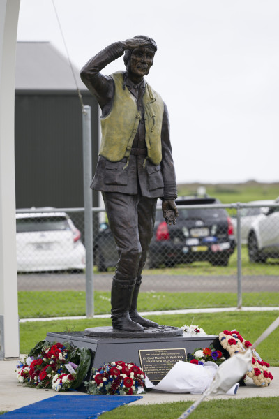 A bronze statue of man giving a salute, with wreaths around its base.