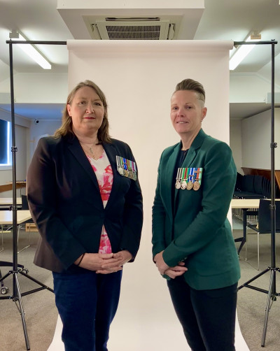 Rebecca Brierton and Ange Coyle stand casually in front of a photography backdrop in a studio