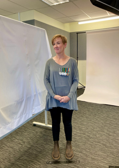 Kelley Waite wearing her medals, standing casually in front of two photography backdrops