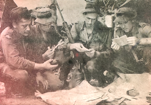 Bill kneeling with 3 other men around a tin and documents that were found.