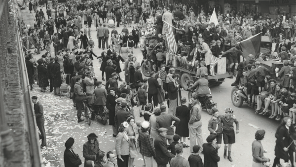 A parade of hundreds of people celebrating in the street. There are people piled onto trucks, with flags and banners.