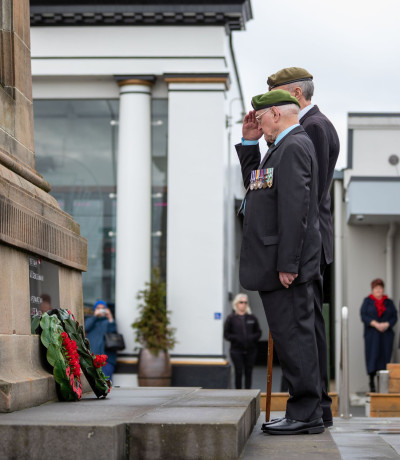 Two men salute wreaths at a commemoration